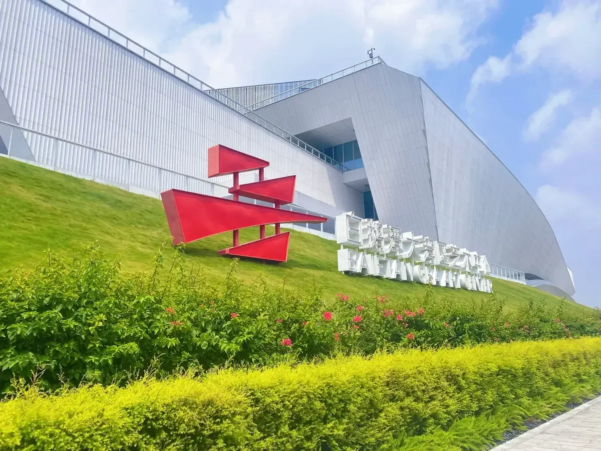 Lush green sloped lawn with the red sculptural center emblem in front of the white modern pavilion