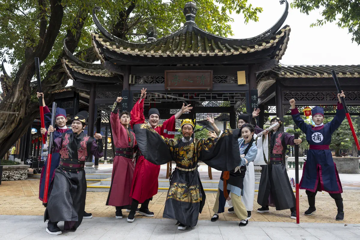 Performers dressed in historical Song Dynasty magistrate robes and imperial guard attire in front of Qingxin Pavilion at Baomo Garden