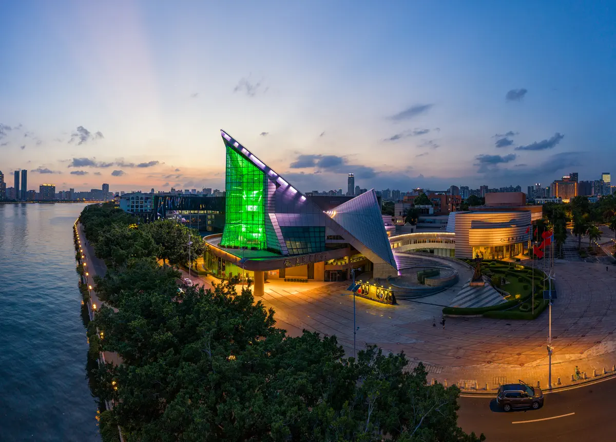 Night view of Xinghai Concert Hall and Guangdong Museum of Art illuminated with emerald and violet lights along the Pearl River