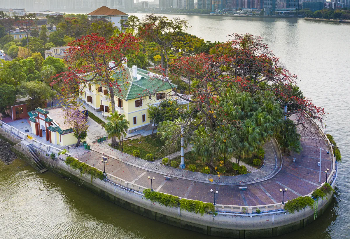 Historic Republican-era yellow villa with green glazed tiles and blooming red kapok trees at the western tip of Ersha Island