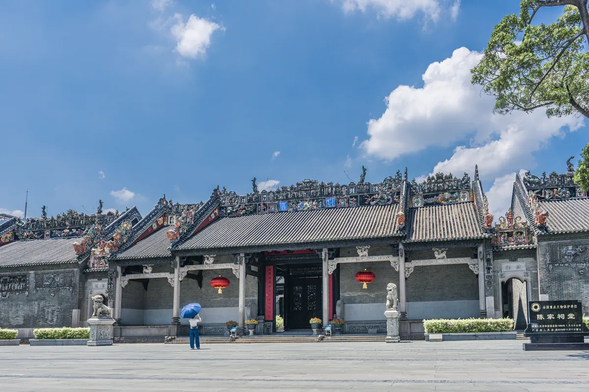 Front monumental entrance facade of Chen Clan Ancestral Hall with granite steps, stone lions, red lanterns, and ornamental porcelain roof ridge under blue sky