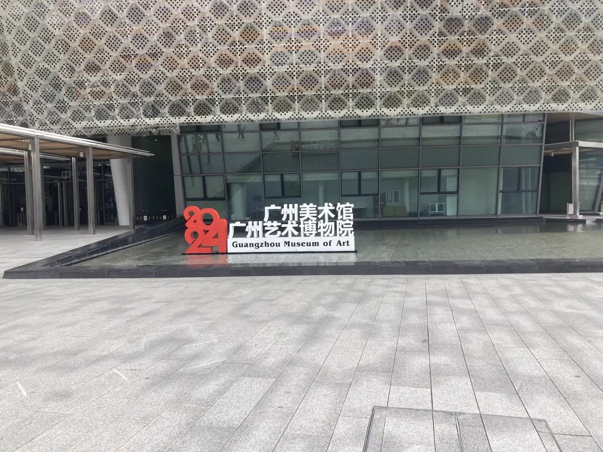 Main ground level signage reading Guangzhou Museum of Art placed in front of reflecting waters and the glass curtain wall