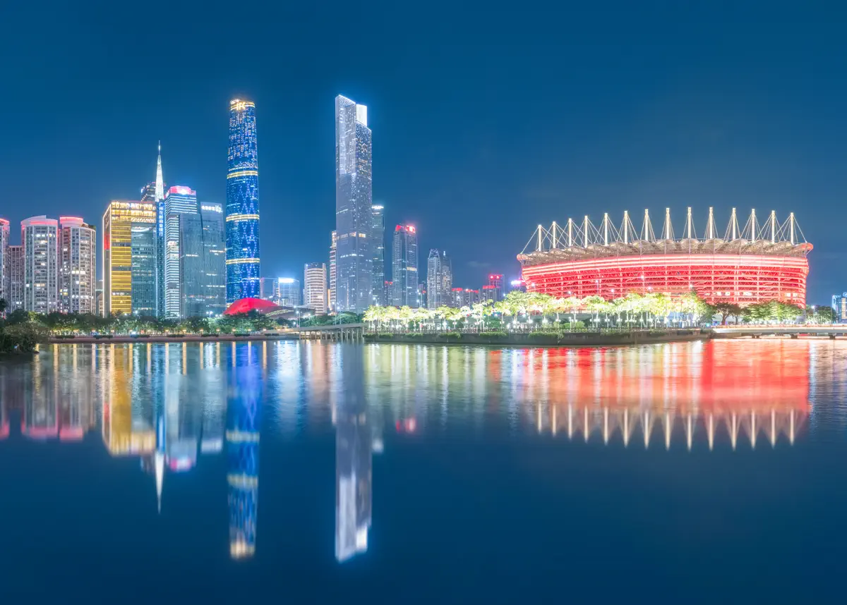 Vibrant night reflection of Haixinsha Asian Games grandstand illuminated in red lights with the illuminated twin towers of Zhujiang New Town across the water