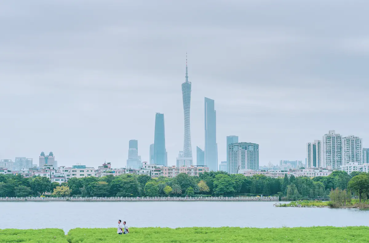 Iconic flower-and-tower viewpoint at Haizhu Lake showing blooming meadows, calm lake waters, resting egrets, and Canton Tower
