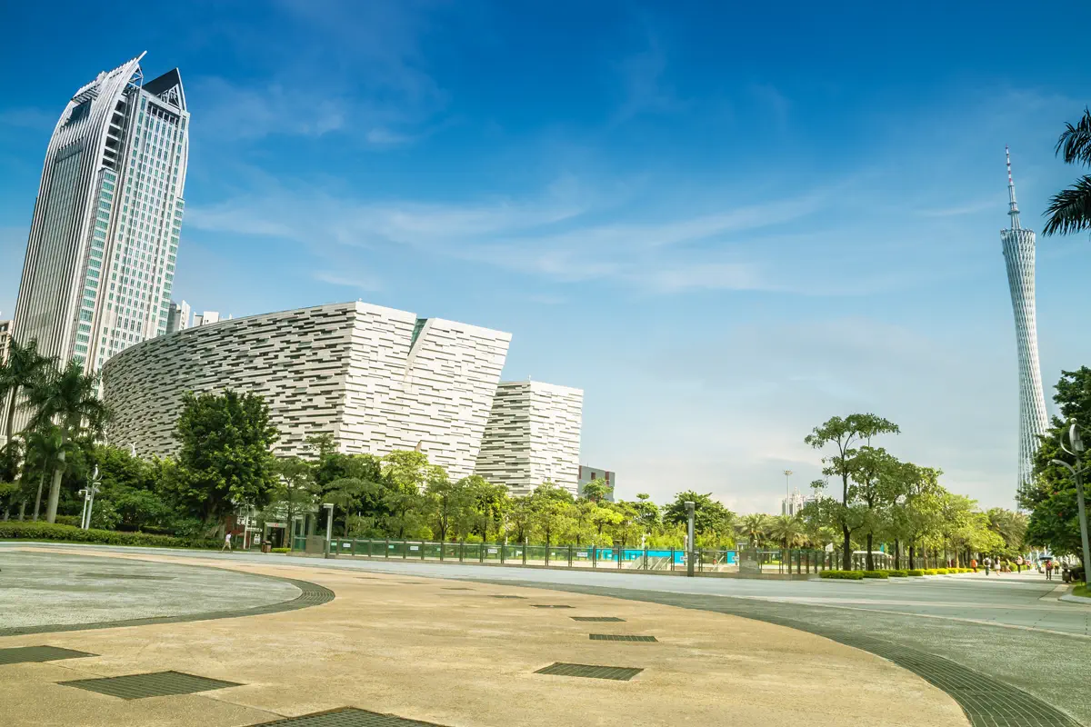 Angled view of Guangzhou Library resembling stacked open books beside modern high-rises with Canton Tower in the distant sky