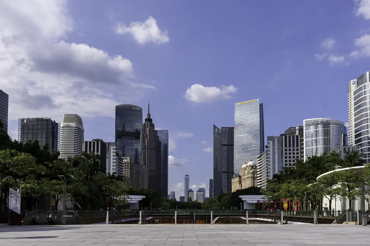 Wide view looking down the central pedestrian promenade of Huacheng Square toward the sunken mall entrance and modern office skyline