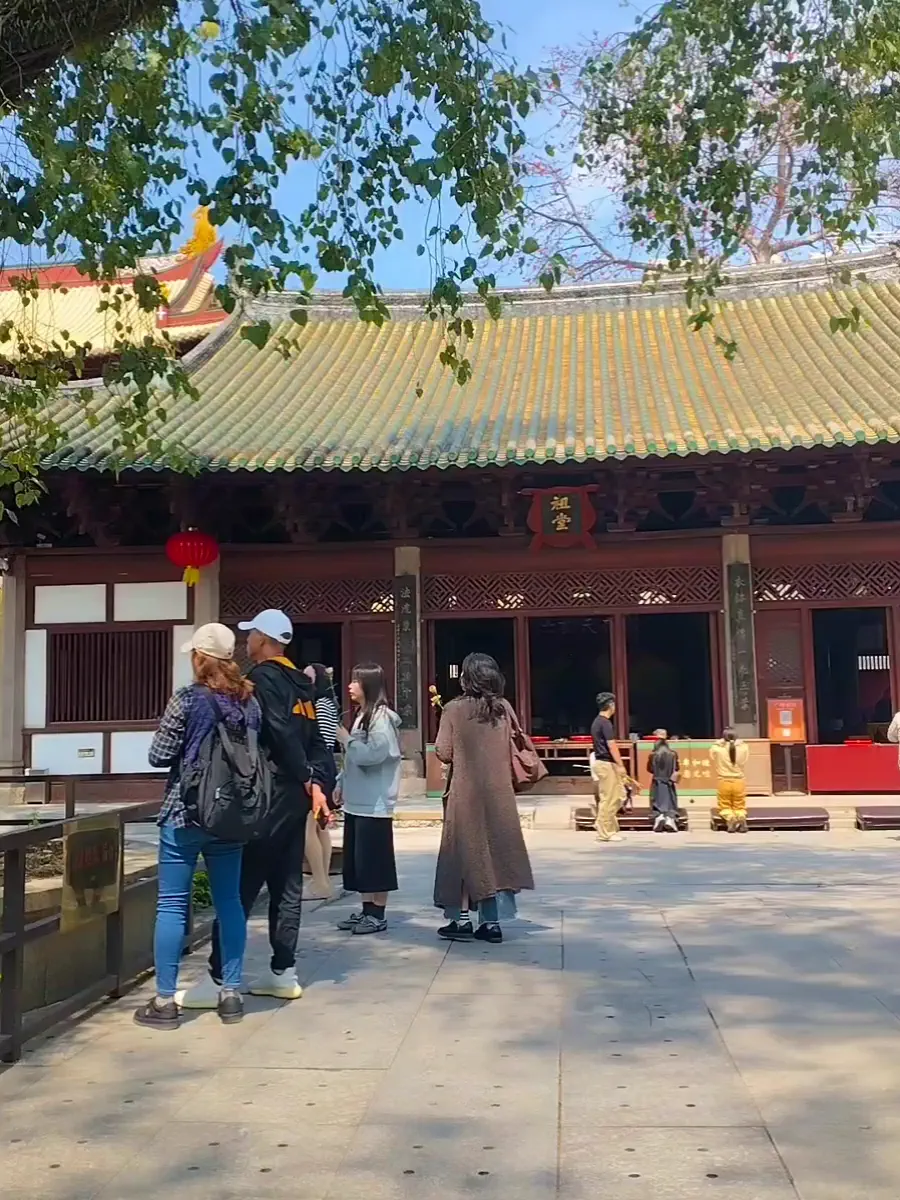 Courtyard of Hualin Temple shaded by mature green trees with temple roofs and visiting locals
