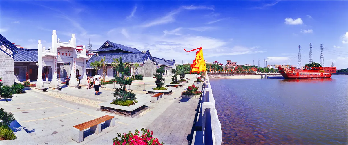 Wide panoramic view of Huangpu Ancient Port riverside plaza featuring a traditional red wooden merchant ship and yellow banners