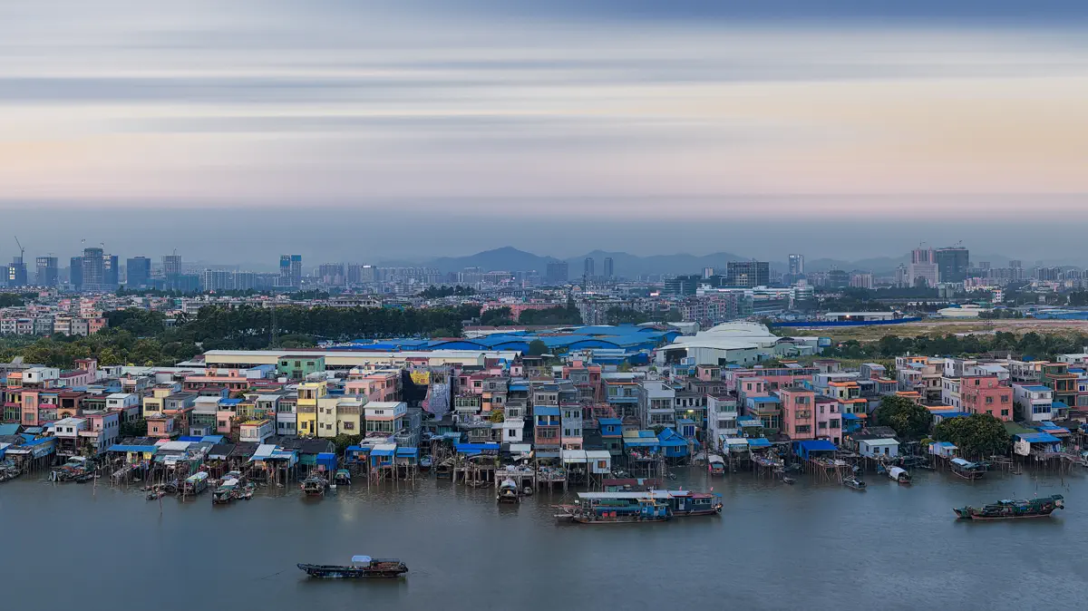 Riverside village houses on stilts along the Pearl River with small workboats moored along the tidal banks