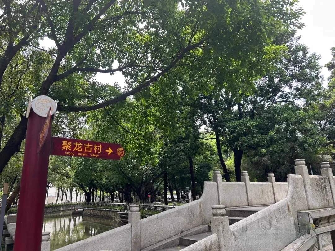 Arched granite stone bridge crossing Dachongkou Canal with a directional red signpost to Julong Ancient Village