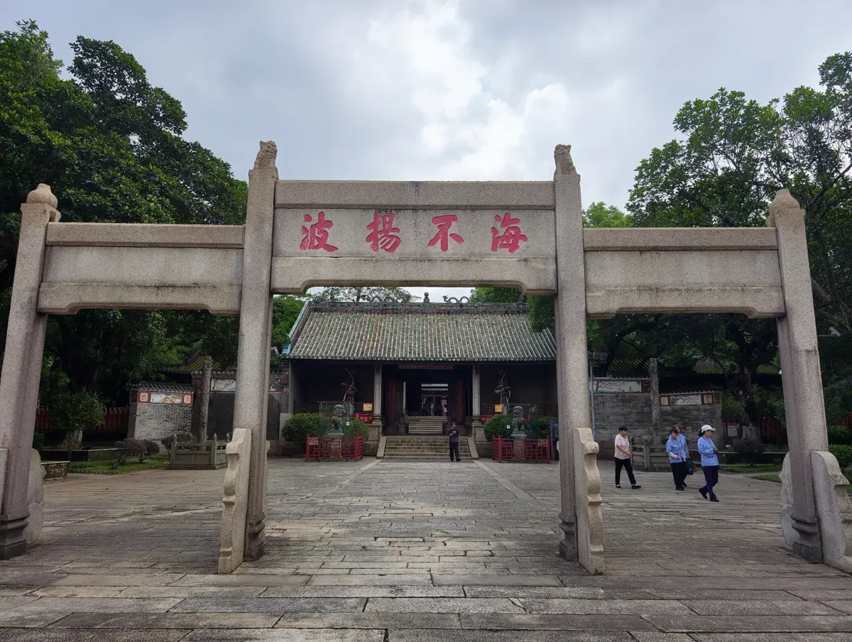 Four-pillar granite ceremonial archway inscribed with Hai Bu Yang Bo in red calligraphy before ancient banyan groves