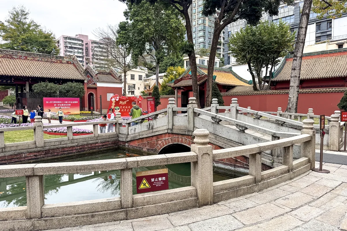 Crescent shaped Pan Pond with single-arch stone bridge, reflections in quiet green water, and vermilion perimeter walls at Panyu Confucian Temple