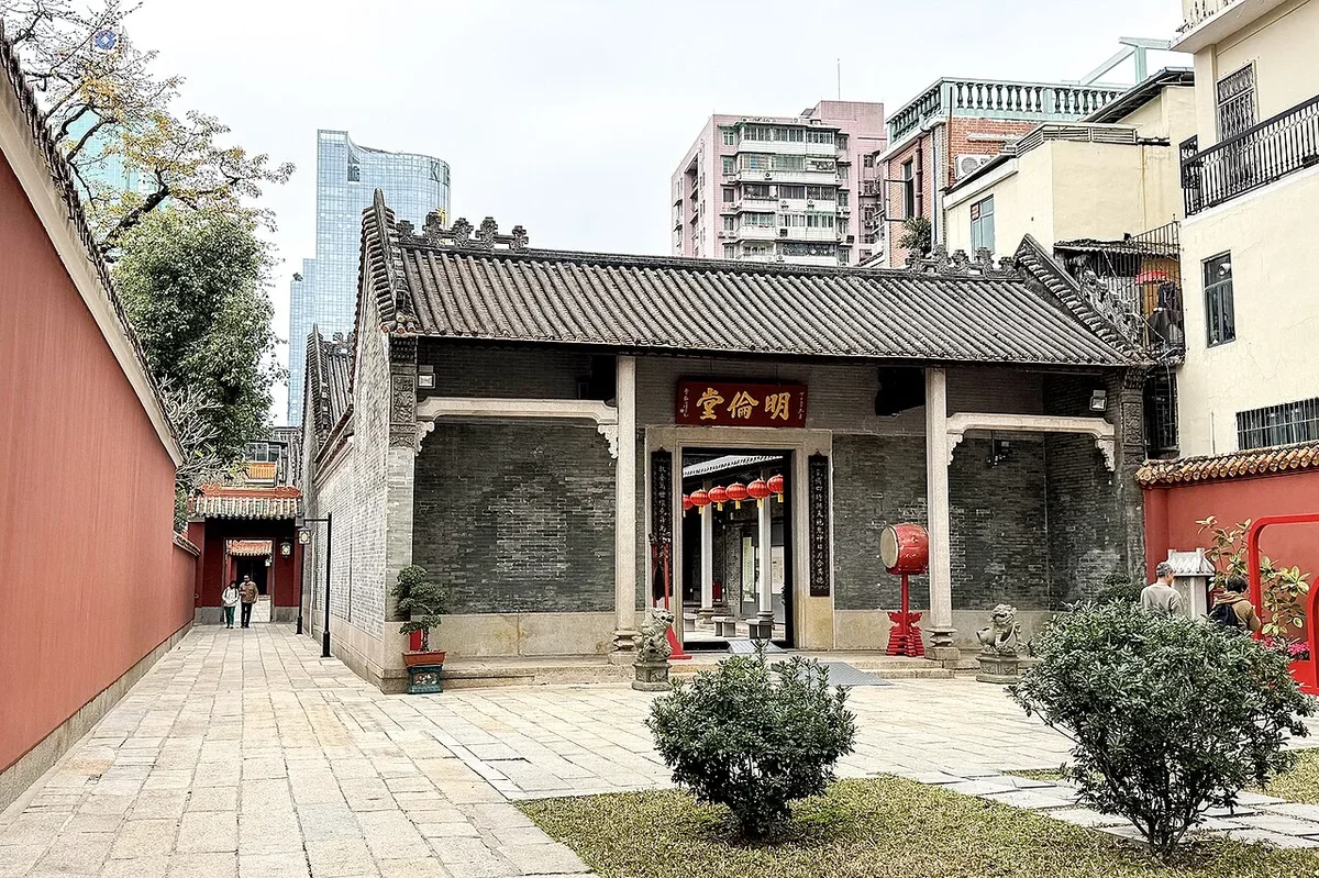 Wok-ear gable brick wall exterior of Minglun Hall with red screen wall corridor and guardian stone lions