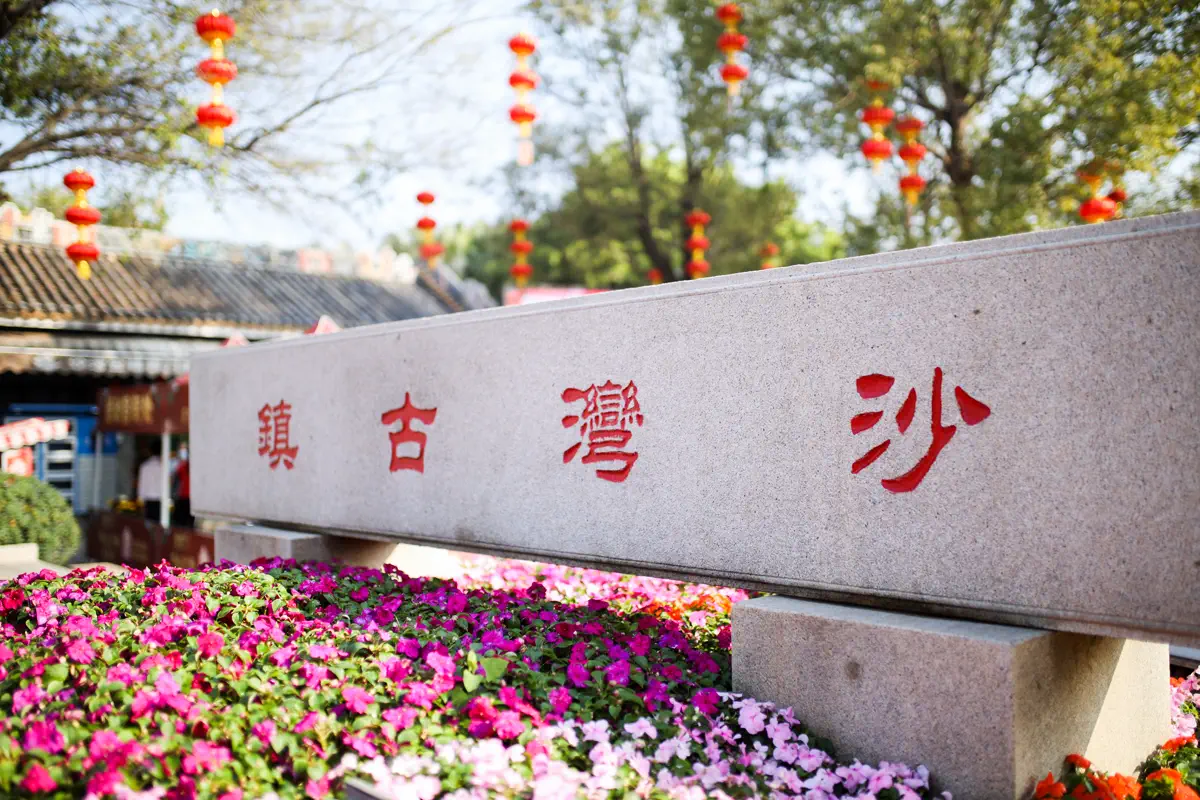 Carved stone entrance marker of Shawan Ancient Town surrounded by flowerbeds
